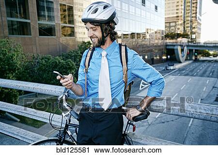 Stock Image - Caucasian businessman with bicycle using cell phone. Fotosearch