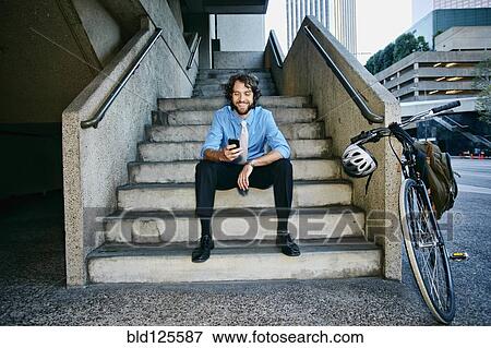 Stock Photo - Caucasian businessman with bicycle using cell phone. Fotosearch