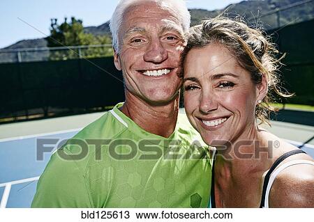 Stock Image - Caucasian couple hugging on tennis court. Fotosearch