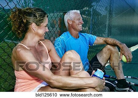 Stock Image - Caucasian couple sitting on tennis court. Fotosearch