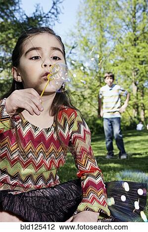 Stock Image - Caucasian girl blowing bubbles in park. Fotosearch