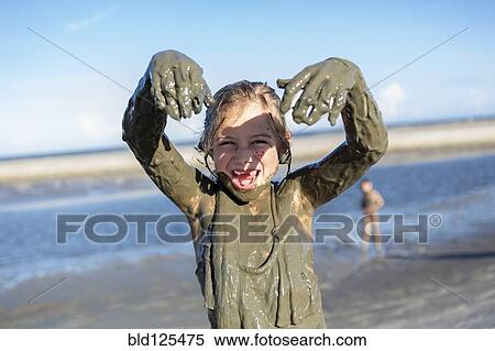Stock Photography - Caucasian girl playing in mud on beach. Fotosearch