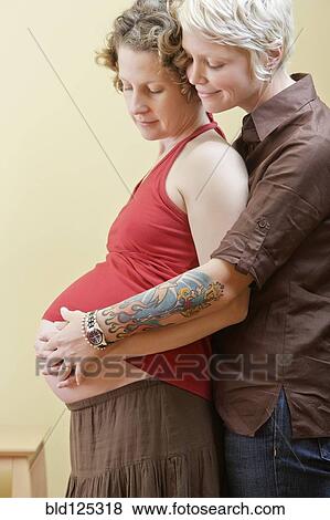 Stock Photo - Caucasian lesbian couple holding pregnant belly. Fotosearch