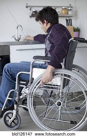 Stock Photo - Caucasian man in wheelchair using kitchen sink. Fotosearch