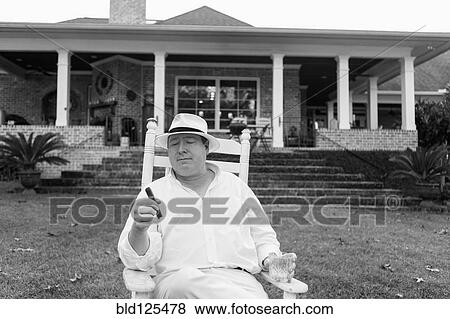 Stock Photo - Caucasian man relaxing with cigar in yard. Fotosearch