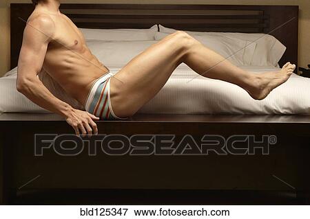 Stock Photo - Caucasian man sitting on bed. Fotosearch