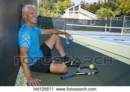 Stock Image - Caucasian man sitting on tennis court. Fotosearch