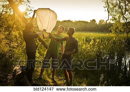 Stock Photo - Caucasian men launching floating lantern outdoors. Fotosearch