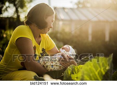 Stock Image - Caucasian mother holding baby girl in garden. Fotosearch