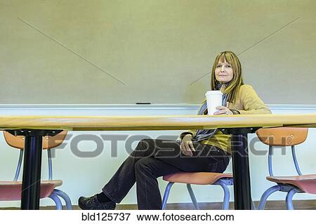 Stock Photo - Caucasian professor sitting at table in classroom. Fotosearch