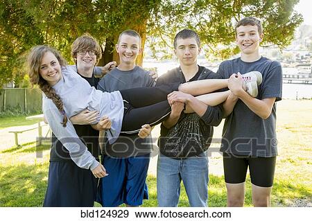 Stock Photo - Caucasian teenage boys holding girl in park. Fotosearch