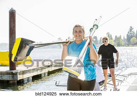 Stock Photography - Caucasian teenage girls carrying oars on dock. Fotosearch