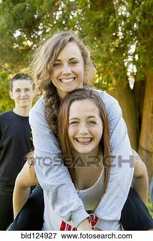 Stock Photo - Caucasian teenage girls piggybacking outdoors. Fotosearch