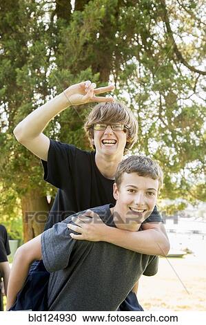 Stock Image - Caucasian teenage piggybacking in park. Fotosearch