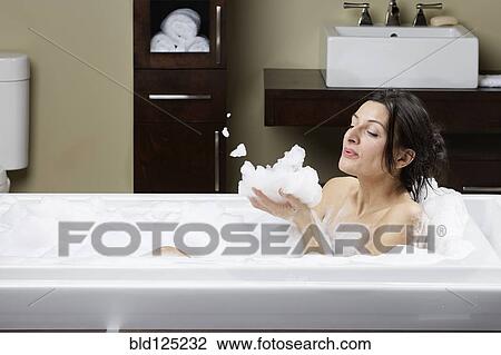 Stock Image - Caucasian woman blowing bubbles in bubble bath. Fotosearch