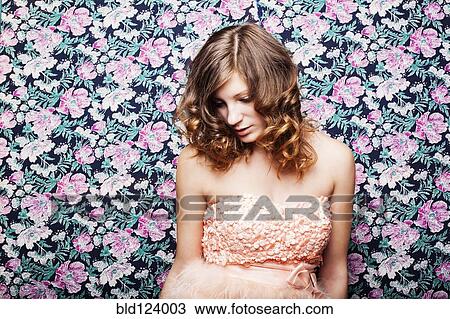 Stock Image - Caucasian woman in pink dress by floral wallpaper. Fotosearch