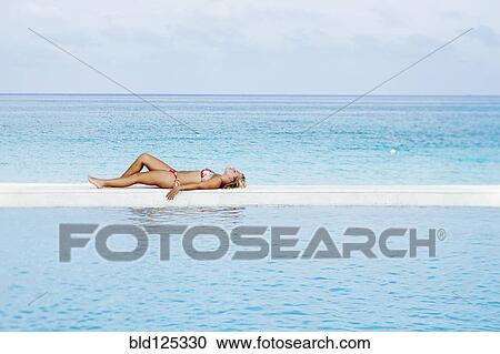Stock Image - Caucasian woman laying by infinity pool. Fotosearch