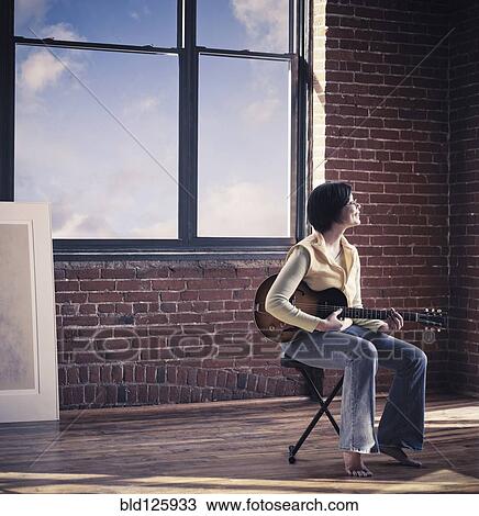 Stock Image - Caucasian woman playing guitar in living room. Fotosearch