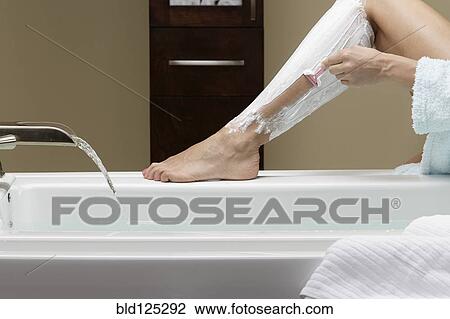 Stock Image - Caucasian woman shaving her legs at bathtub. Fotosearch