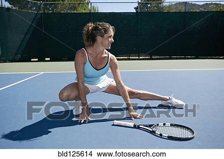 Picture - Caucasian woman stretching on tennis court. Fotosearch