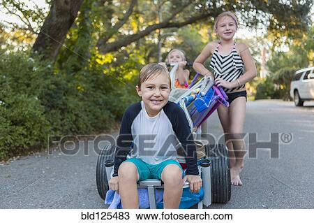 Stock Image - Children in swimsuits pushing cart on rural road. Fotosearch