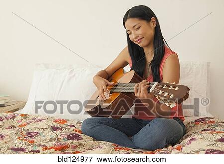 Stock Photo - Chinese woman playing guitar on bed. Fotosearch