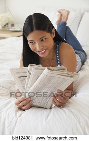 Stock Image - Chinese woman reading newspaper on bed. Fotosearch