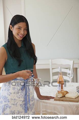 Stock Image - Chinese woman setting table in dining room. Fotosearch