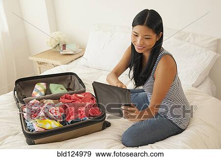 Stock Photo - Chinese woman using digital tablet and packing suitcase. Fotosearch