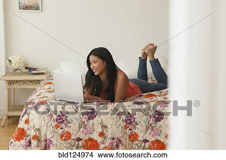 Picture - Chinese woman using laptop on bed. Fotosearch