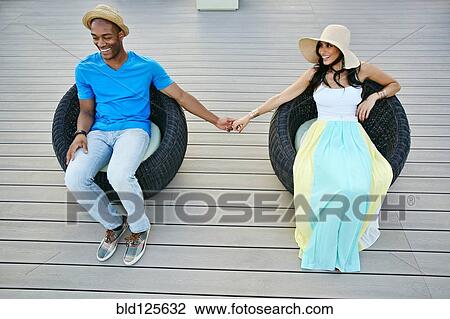 Stock Image - Couple holding hands in wicker chairs. Fotosearch