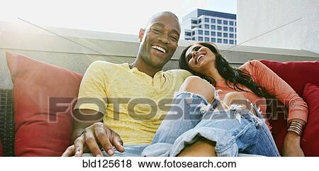 Stock Photo - Couple relaxing on sofa on urban balcony. Fotosearch