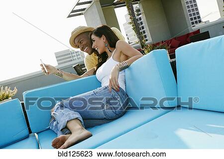 Stock Image - Couple taking self-portrait on sofa on urban balcony. Fotosearch
