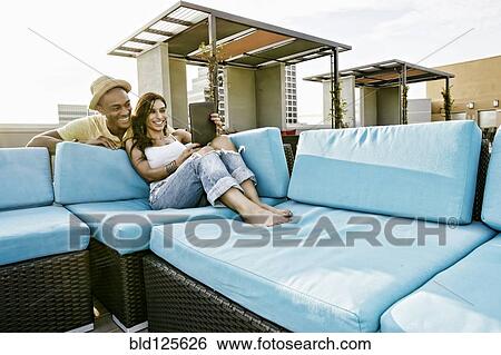Couple using digital tablet on sofa on urban rooftop View Large Photo Image Stock Photograph - Couple using digital tablet on sofa on urban rooftop. Fotosearch