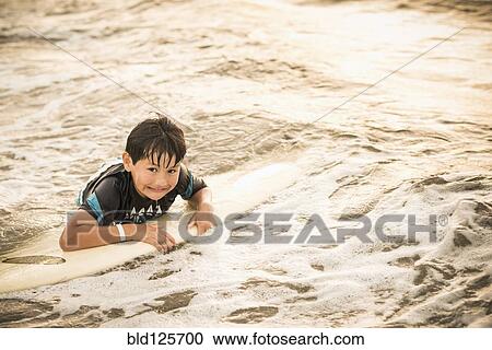 Stock Image - Hispanic boy floating on surfboard in ocean. Fotosearch