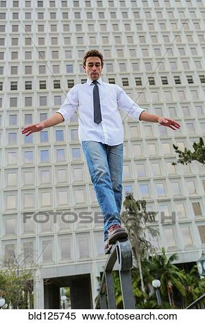 Stock Photography - Hispanic businessman balancing on urban railing. Fotosearch