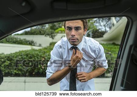 Stock Photo - Hispanic businessman checking his tie in car door mirror. Fotosearch