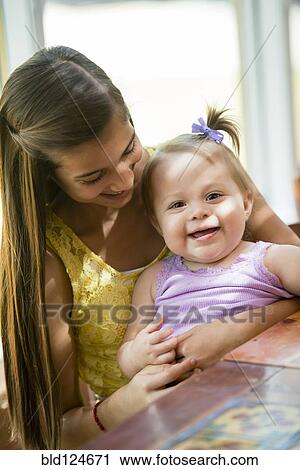 Hispanic girl holding toddler sister at table View Large Photo Image Stock Image - Hispanic girl holding toddler sister at table. Fotosearch