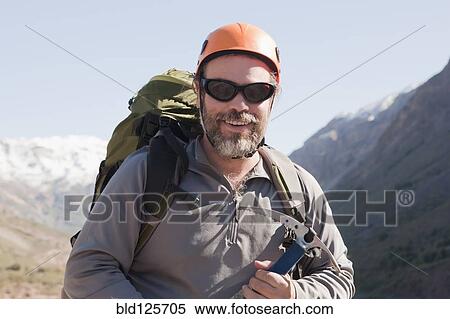 Stock Photography - Hispanic hiker carrying ice ax in mountains. Fotosearch