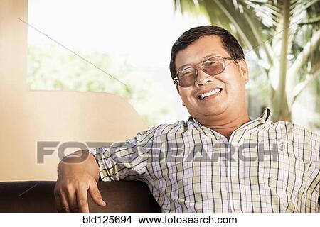 Picture - Hispanic man smiling on sofa. Fotosearch
