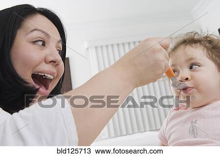 Stock Image - Hispanic mother feeding baby girl. Fotosearch