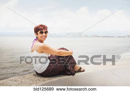 Hispanic woman sitting on stone wall overlooking beach View Large Photo Image Stock Photo - Hispanic woman sitting on stone wall overlooking beach. Fotosearch