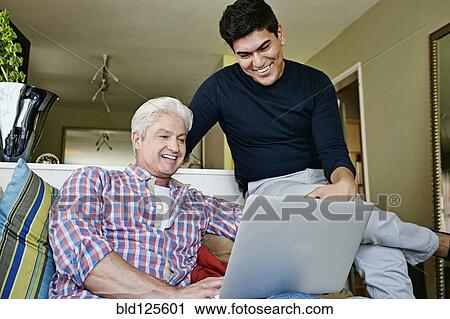 Stock Image - Homosexual couple using laptop in living room. Fotosearch