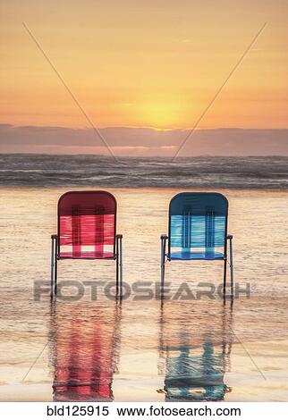 Stock Photography - Lawn chairs in waves on beach at sunset. Fotosearch
