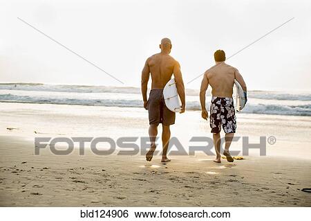 Stock Photograph - Men carrying surfboards on beach. Fotosearch