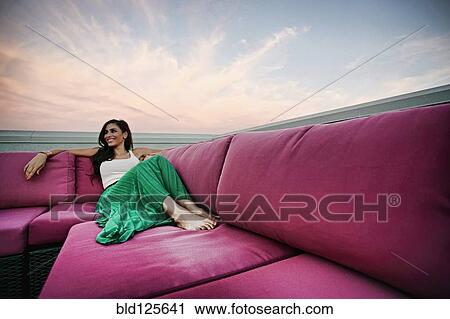 Stock Image - Middle Eastern woman relaxing on sofa outdoors. Fotosearch