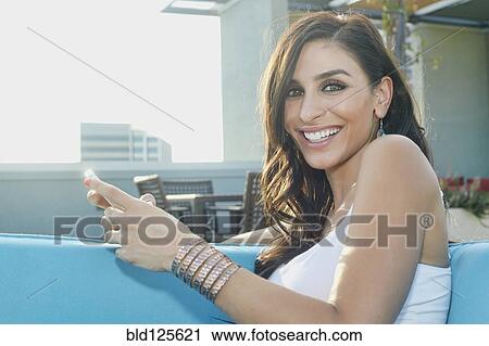 Stock Image - Middle Eastern woman using cell phone on sofa. Fotosearch
