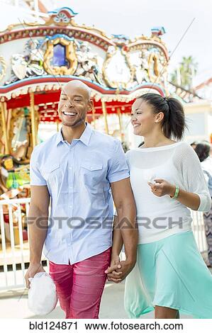 Stock Image - Mixed race couple holding hands at amusement park. Fotosearch
