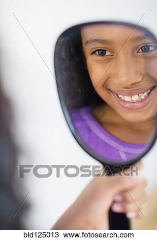 Stock Image - Mixed race girl admiring herself in mirror. Fotosearch