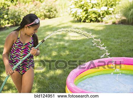 Stock Image - Mixed race girl filling wading pool in backyard. Fotosearch